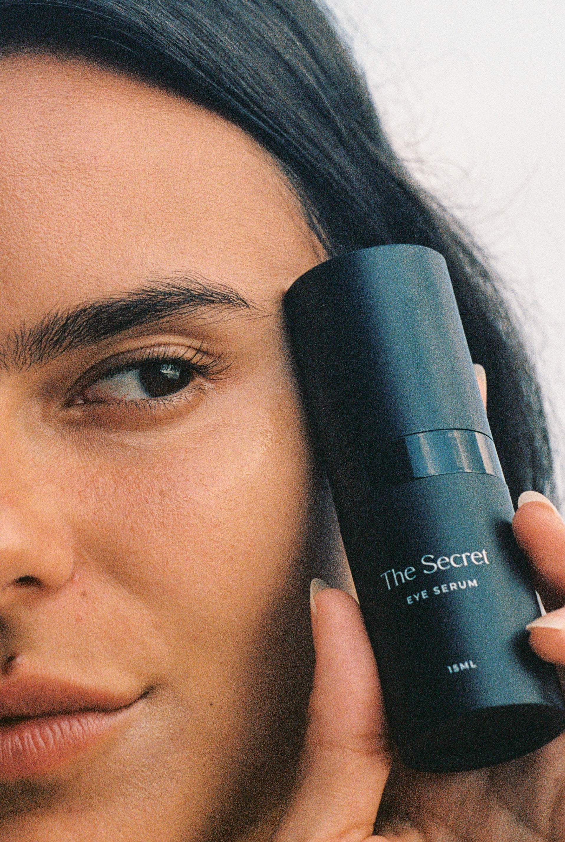 A woman holding The Secret Skincare's Brightening Eye Serum, showcasing its packaging while highlighting its role in skincare.
